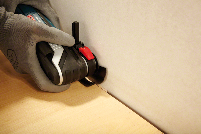 一名穿戴安全裝備的人員使用電動工具在牆邊切割木材。