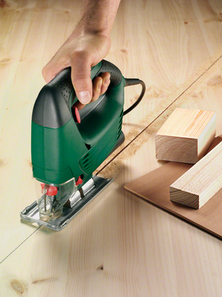 一名工人引導拼圖鋸沿著標記線切割膠合板。.