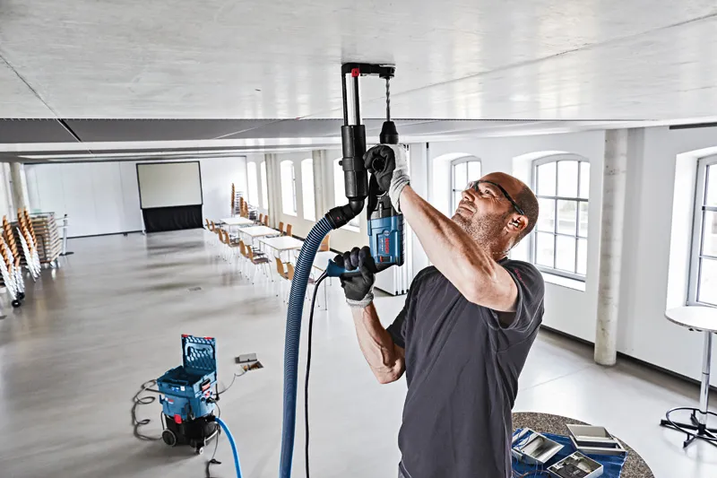 一名配戴安全設備的人員正在用除塵系統鑽入天花板。.