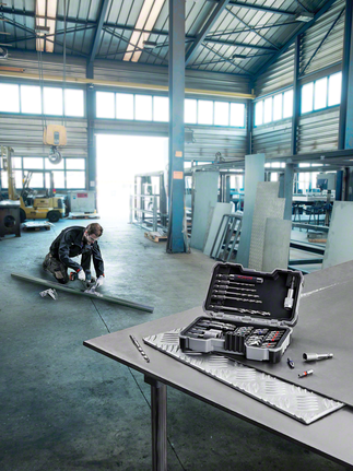 一名穿戴安全裝備的人員在工作台上用鑽頭測量一塊金屬板。