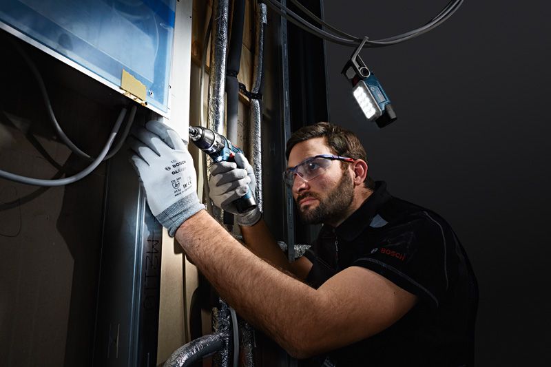 一名佩戴安全設備的人正在牆上鑽孔，無線燈照亮了工作空間。.