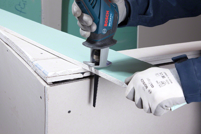 一名配戴安全設備的工人正在用往復鋸切割乾牆。.