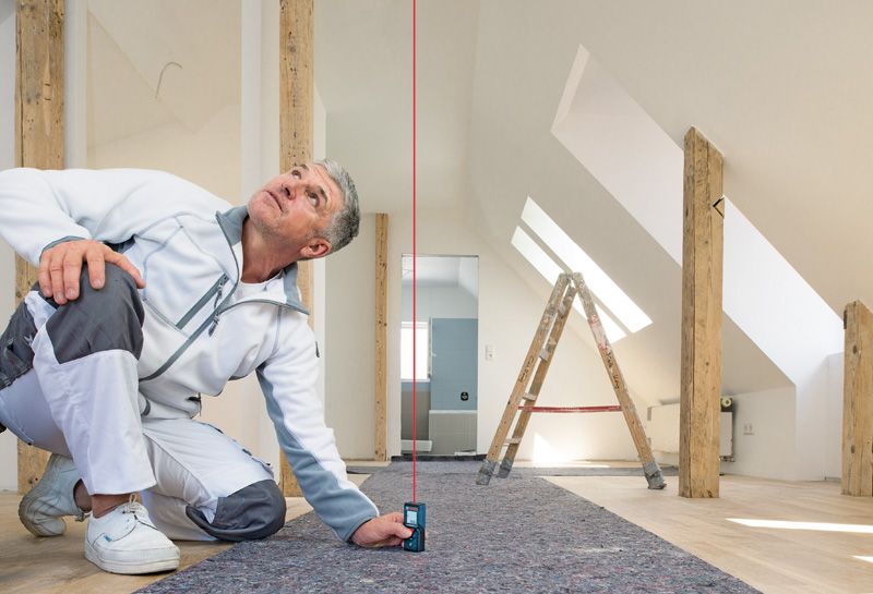 身穿工作服的工作人員使用雷射測量儀檢查裝修後的房間內的垂直距離。.