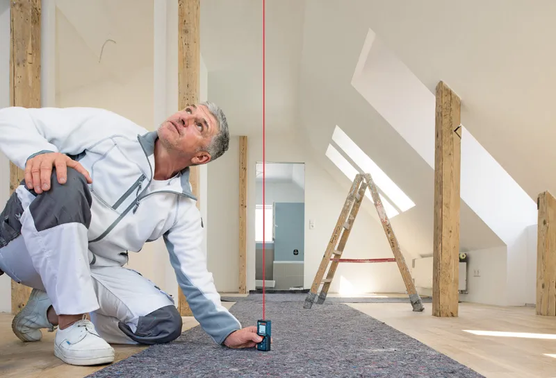 一名男子使用雷射測量儀檢查明亮閣樓房間內的垂直對齊情況。