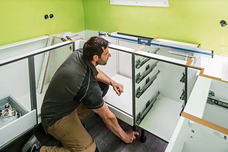 一個人在櫃檯上使用數位測斜儀安裝櫥櫃。.