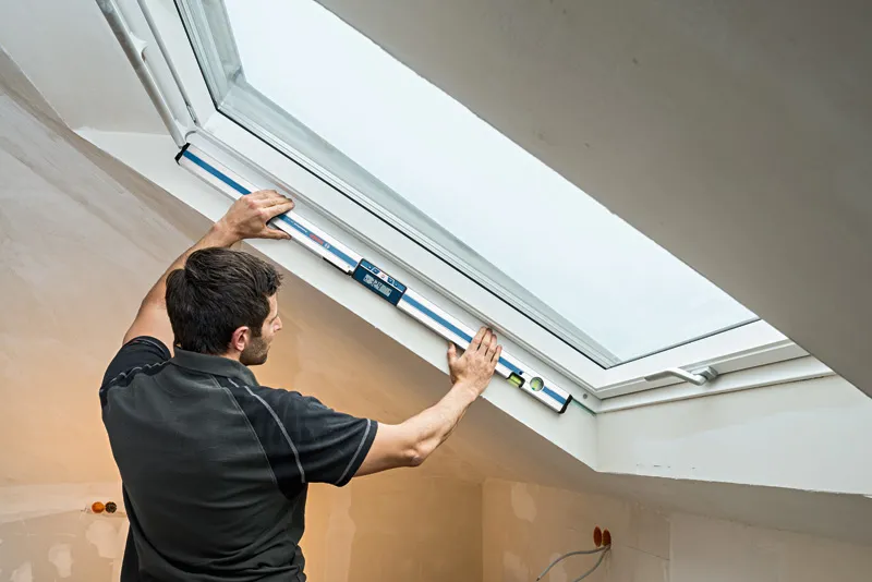 一名人員在裝修完畢的閣樓房間內使用數位測斜儀測量窗戶角度。.