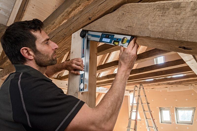 人們在木屋頂下用數位測斜儀檢查木樑的角度。.