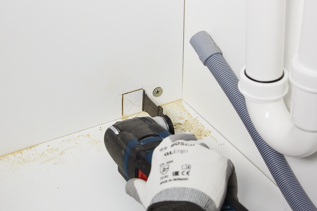 工人配戴安全設備，用電動工具在櫃子上切出一個方形開口。.