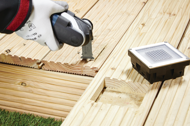 工人配戴安全設備，使用多功能工具在木質甲板上切割出凹槽。.