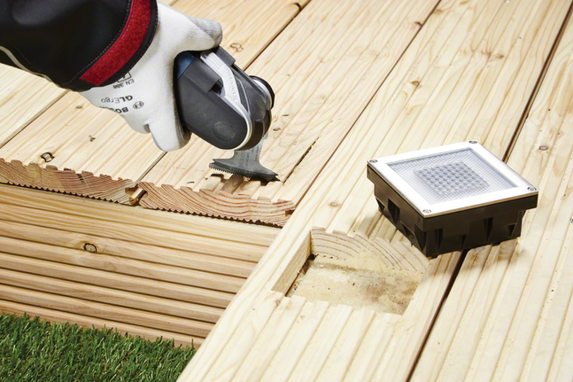 佩戴安全設備的人員正在切割嵌入式燈具附近的木質甲板面板。.