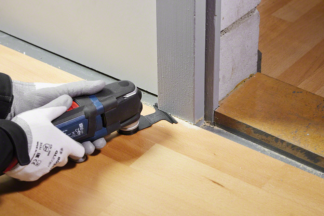 配戴安全設備的人員使用電動工具修剪門框旁的木地板。.