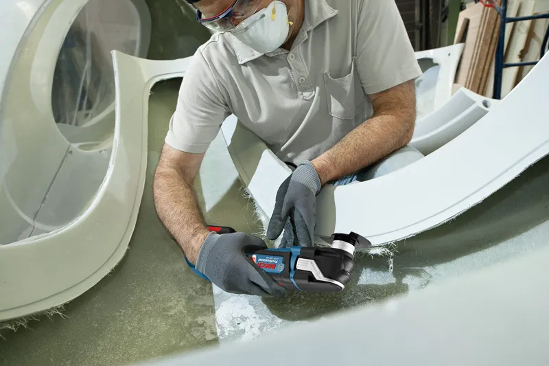 一名佩戴安全設備的人正在使用無線多功能工具切割玻璃纖維。.