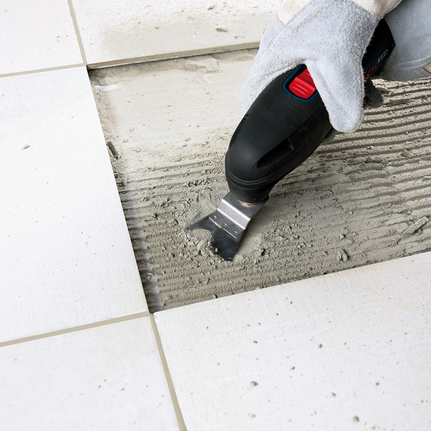 工人佩戴安全設備，使用多功能工具去除地磚之間的黏合劑。.