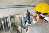 施工期間，一名配戴安全設備的人員正在混凝土天花板上鑽孔。.