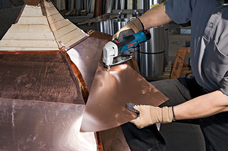 一名配戴安全設備的人員正在使用無線金屬剪剪切金屬板。.