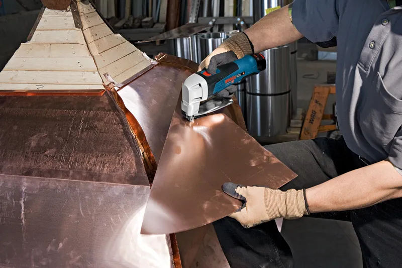 一名配戴安全設備的人員正在使用無線金屬剪剪切金屬板。.