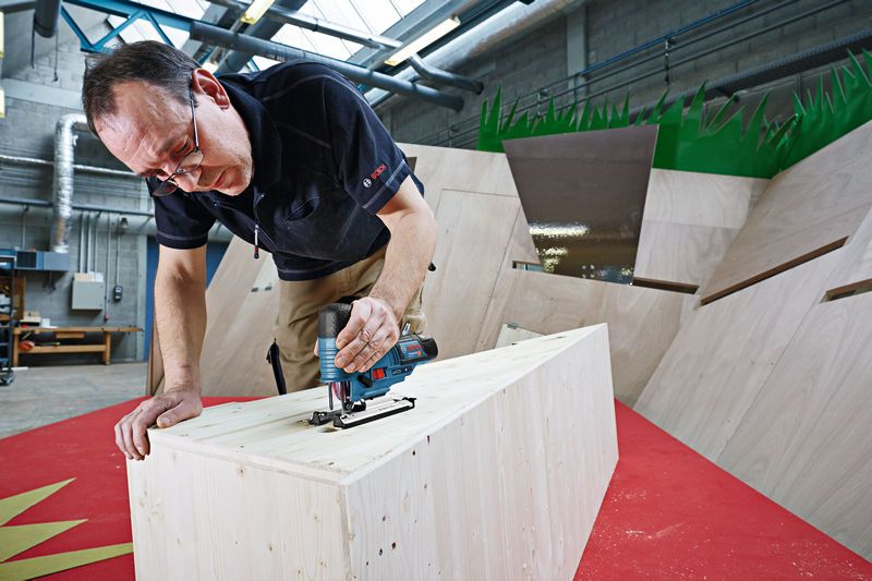 一個人在車間使用無線曲線鋸切割木材。.