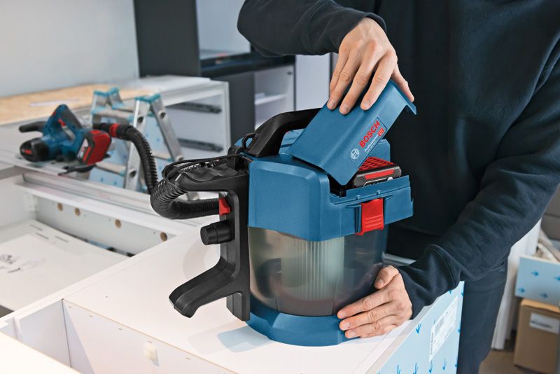 GAS 18V-10 L 一個人將電池插入工作台上的無線除塵器。.