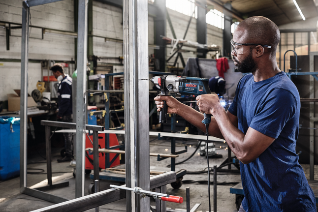 穿著安全設備的人員在工業車間內鑽入金屬框架。.