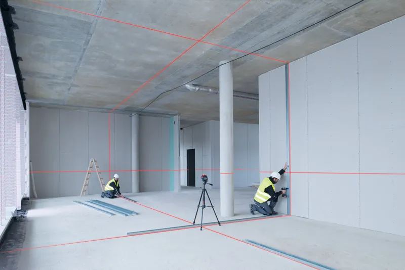 GLL 3-80 兩名配戴安全設備的人員使用雷射調平工具在建築物內調整乾牆。.