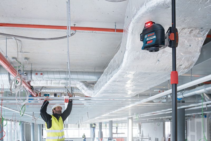 一名配戴安全設備的人員使用雷射調平工具對準天花板框架。.