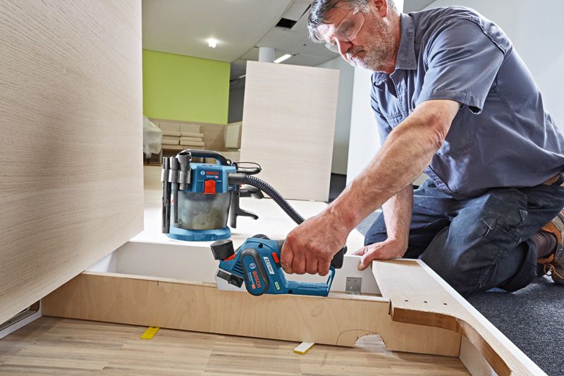 一名配戴安全設備的人員使用無線刨床打磨木板。.