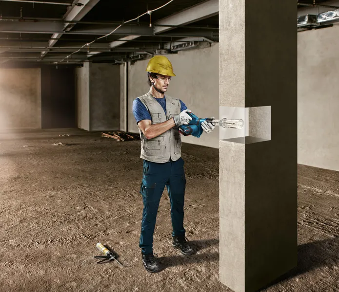 一名穿戴安全裝備的人員正在建築工地鑽探混凝土柱。