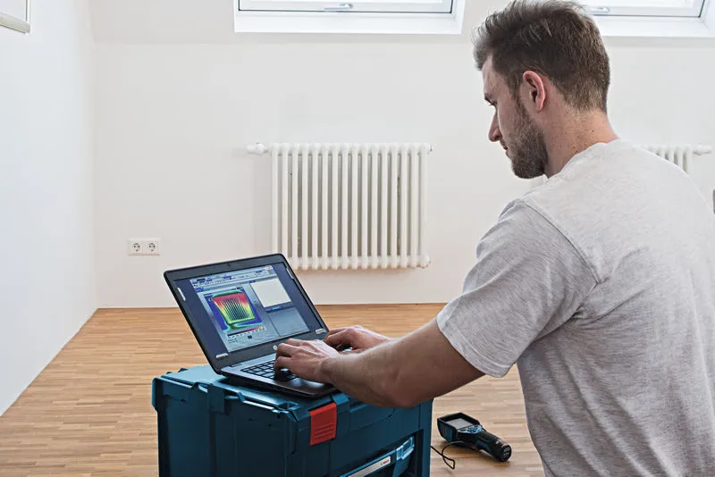 一名人員在裝有散熱器的房間裡用筆記型電腦分析熱像儀數據。.