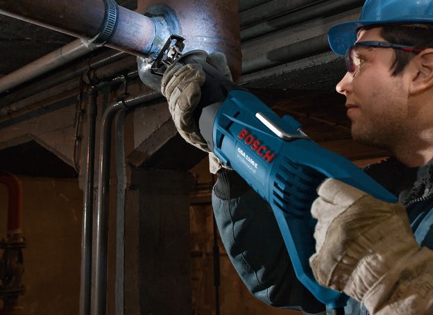 一名配戴安全設備的人員使用往復鋸切割金屬管路。.