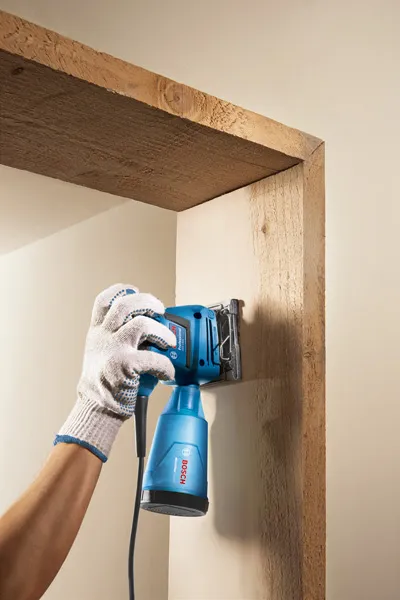 一名配戴安全設備的人員正在使用電動工具打磨木門框。.