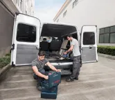 一輛敞篷貨車旁的兩名工人整理工具並使用無線吸塵器。.