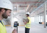 兩名配戴安全設備的人員在大型建築工地內使用雷射測量儀和平板電腦。