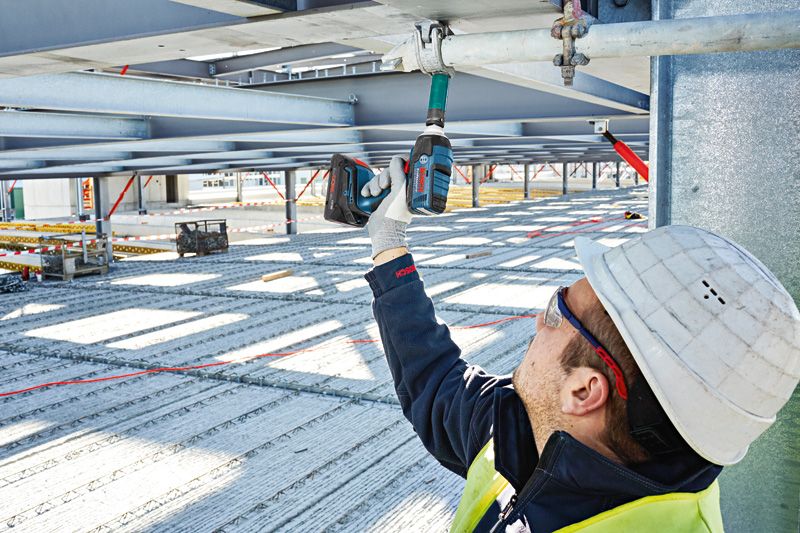 一名配戴安全設備的人員使用無線衝擊扳手來擰動金屬梁。.