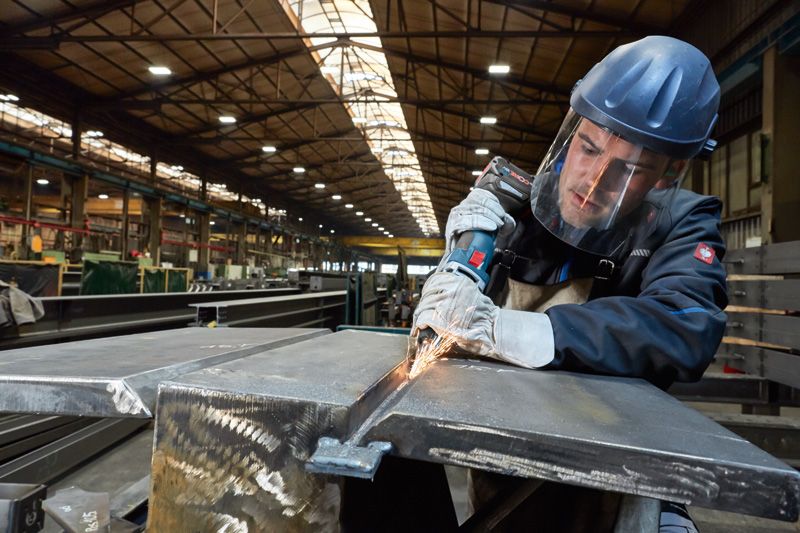 一名配戴安全設備的工人在工廠裡用電動工具磨金屬。.