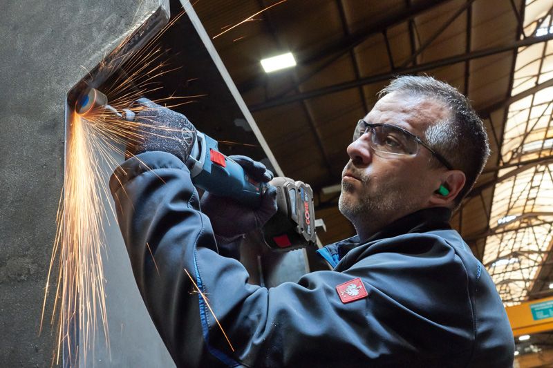 一名佩戴安全設備的人研磨金屬，產生明亮的火花。.