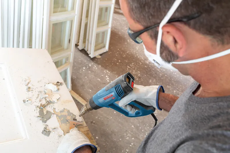 配戴安全設備的人員使用熱風槍剝去門上的油漆。