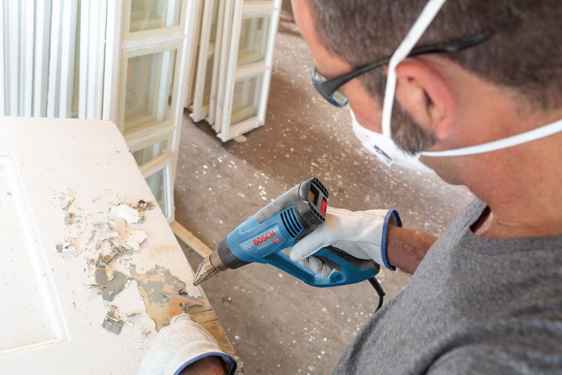 配戴安全設備的人員使用熱風槍剝去門上的油漆。