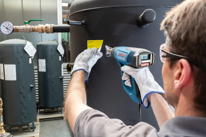 一名配戴安全設備的人員使用熱風槍將標籤貼在大罐上。