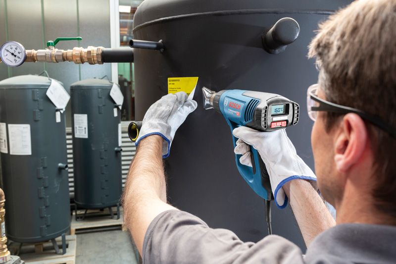 一名配戴安全設備的人員使用熱風槍將標籤貼在大罐上。