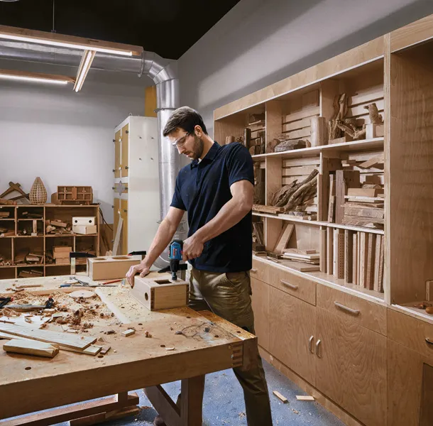 一名配戴安全設備的人員在車間使用無線電鑽對木箱進行鑽孔。.