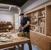 一名佩戴安全設備的人員在木工車間的工作台上鑽孔木頭。