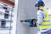 配戴安全設備的人員使用無線旋轉錘在混凝土牆上鑽孔。.