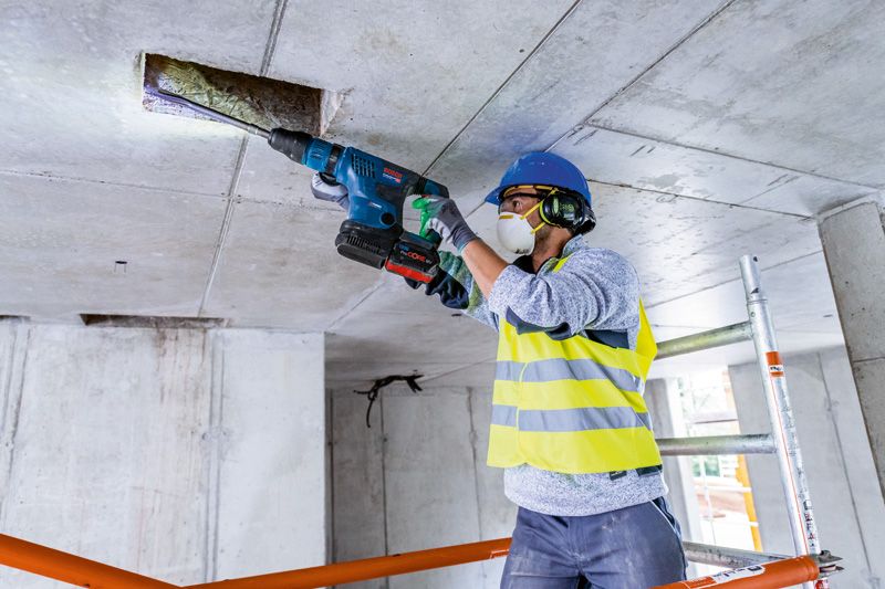 一名穿戴安全裝備的人員使用電錘在混凝土天花板上鑽孔。