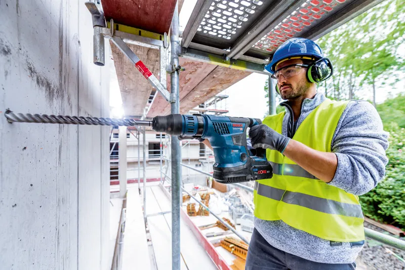 一名佩戴安全設備的人員使用無線旋轉錘在混凝土中鑽孔。.