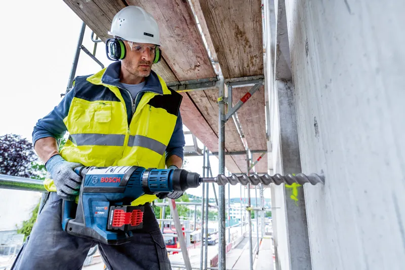 GBH 18V-45 C 一名佩戴安全設備的人員使用無線旋轉錘在混凝土中鑽孔。.