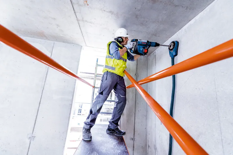 GBH 18V-45 C 一名配戴安全設備的人員使用旋轉錘在混凝土天花板上鑽孔。.
