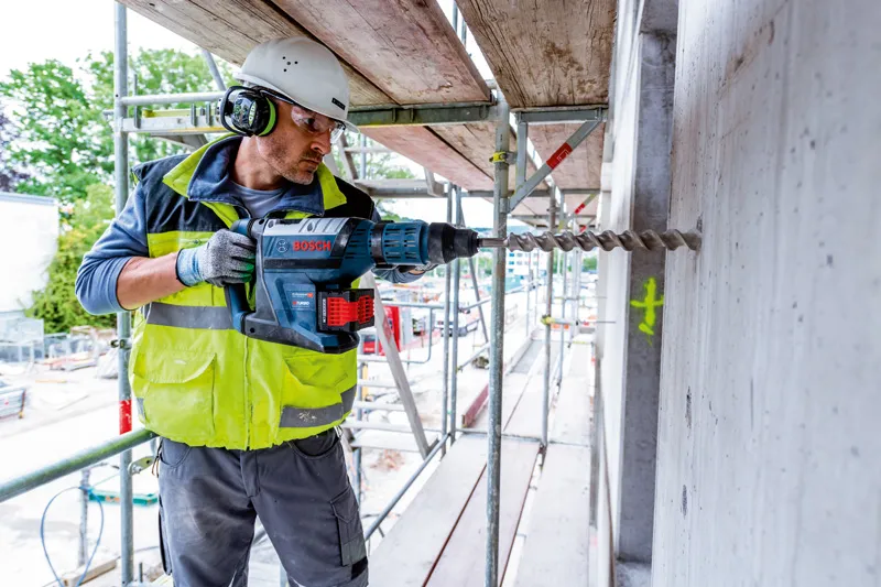 一名佩戴安全設備的人員在建築工地的混凝土牆上鑽孔。.