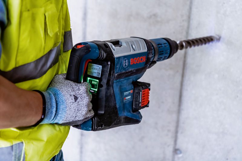 GBH 18V-45 C 一名佩戴安全設備的人員使用大型旋轉錘在混凝土中鑽孔。.