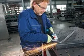 一名佩戴安全設備的工人在車間使用角磨機打磨金屬梁。