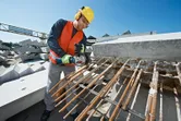 在建築工地上，一名配戴安全設備的工人正在用電動工具切割鋼筋。